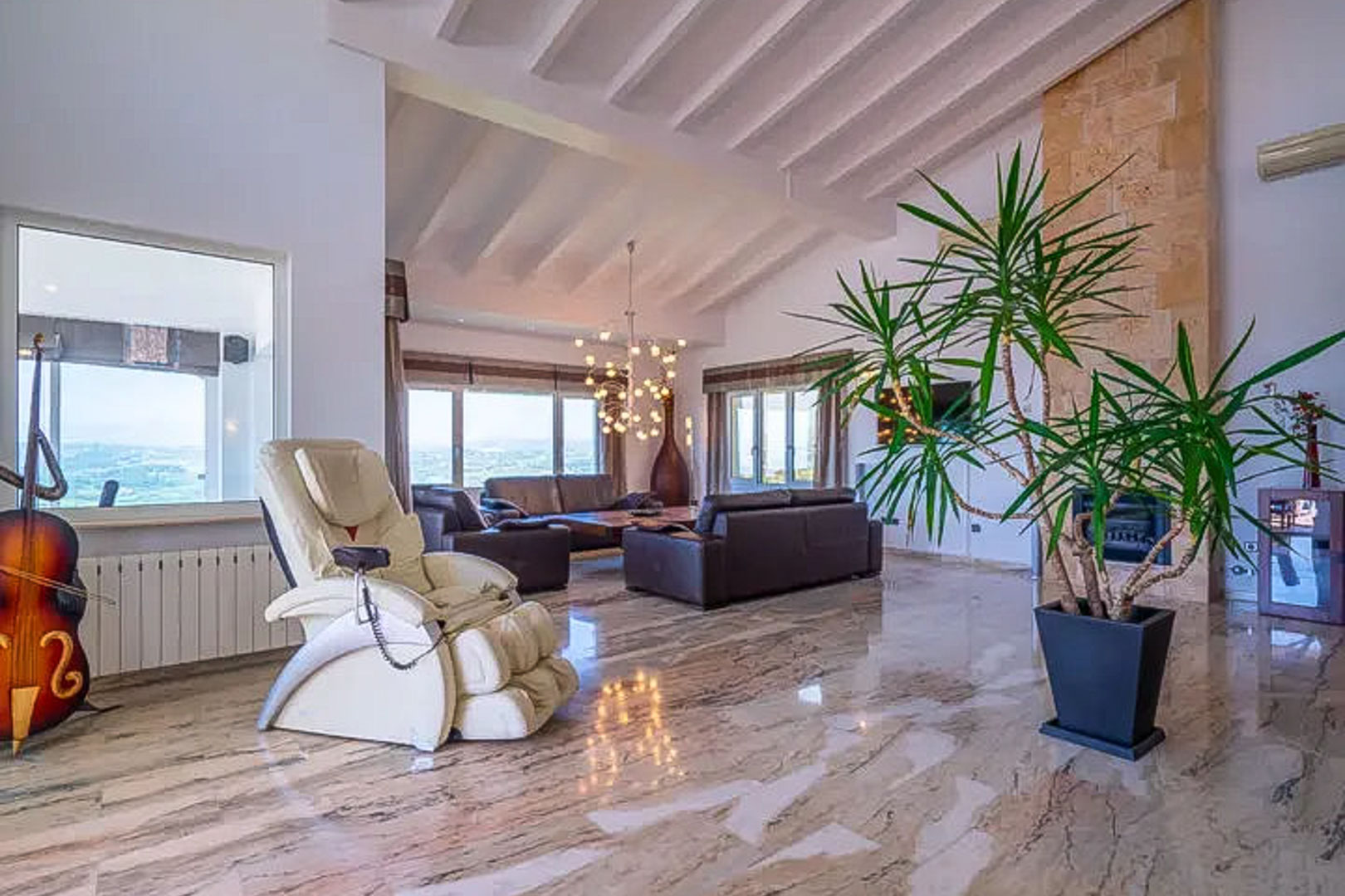 Spacious living room featuring vaulted beamed ceilings, polished marble floors, and a stone fireplace. Large windows offer natural light and views over the Moraira landscape.