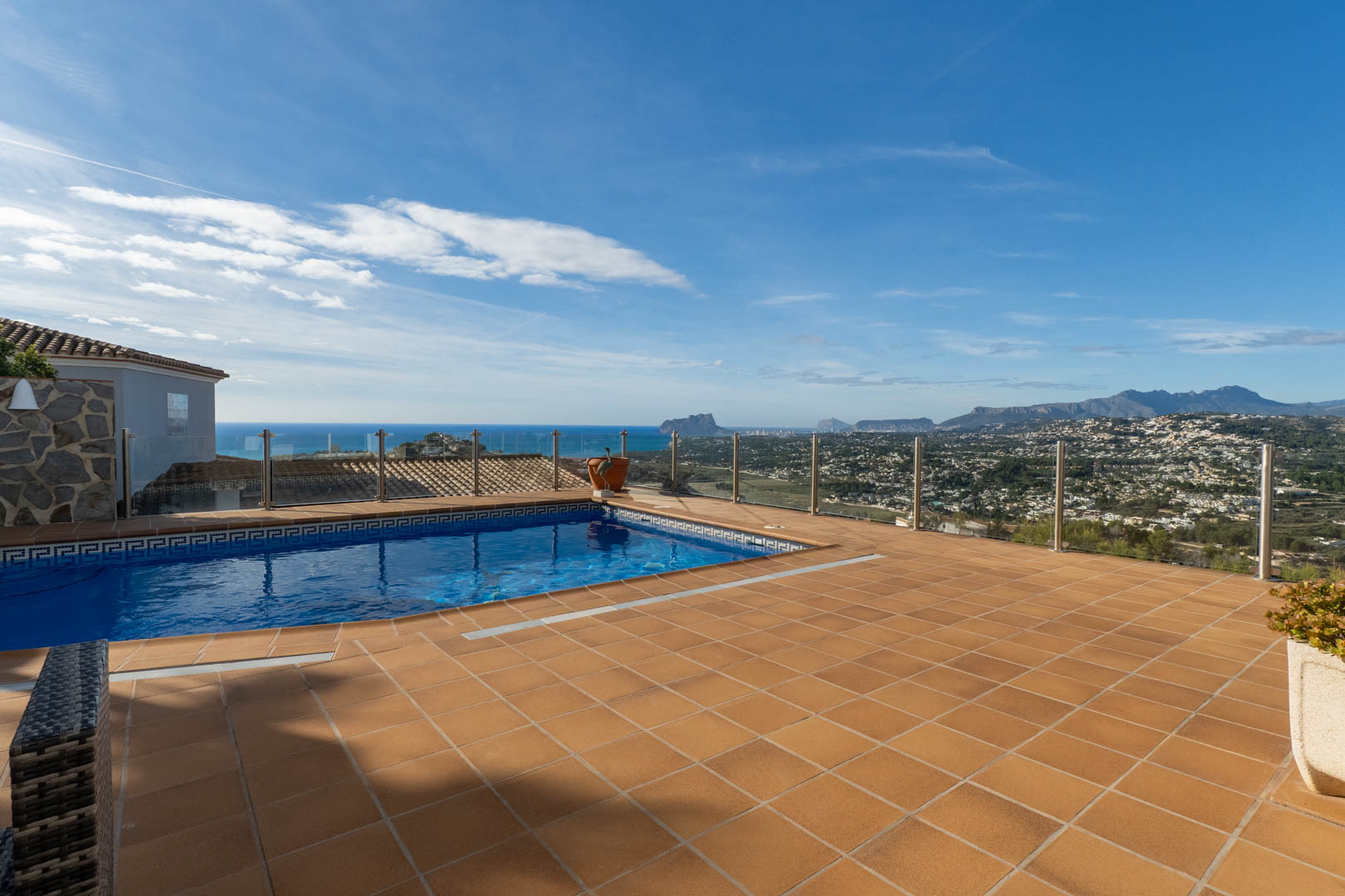 Terracotta-tiled terrace featuring a private pool with glass balustrades, providing unobstructed views of the Mediterranean coastline and the Peñón de Ifach.