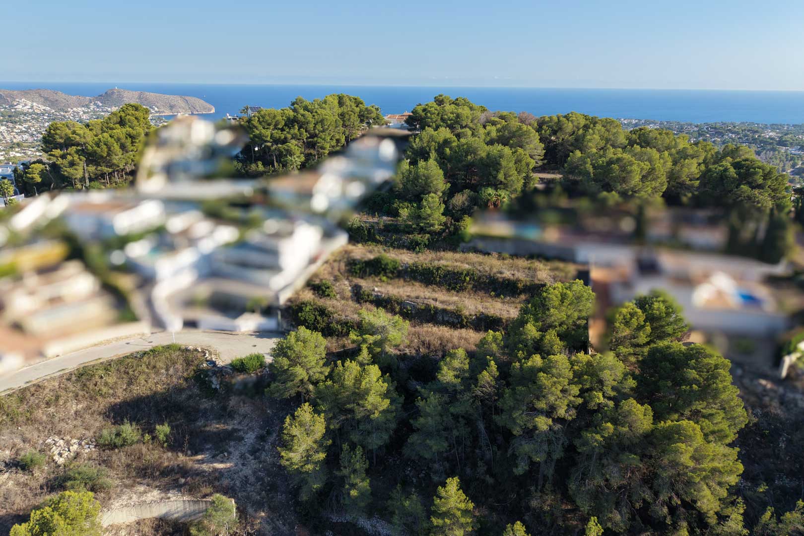 Aerial view of the terraced urban plot, surrounded by dense Mediterranean pines with clear views towards the sea and the Moraira coastline.