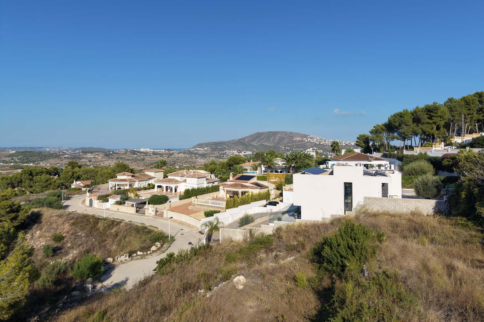 Elevated perspective of a residential neighborhood featuring modern villas, solar installations, and panoramic views of the valley and Mediterranean horizon.