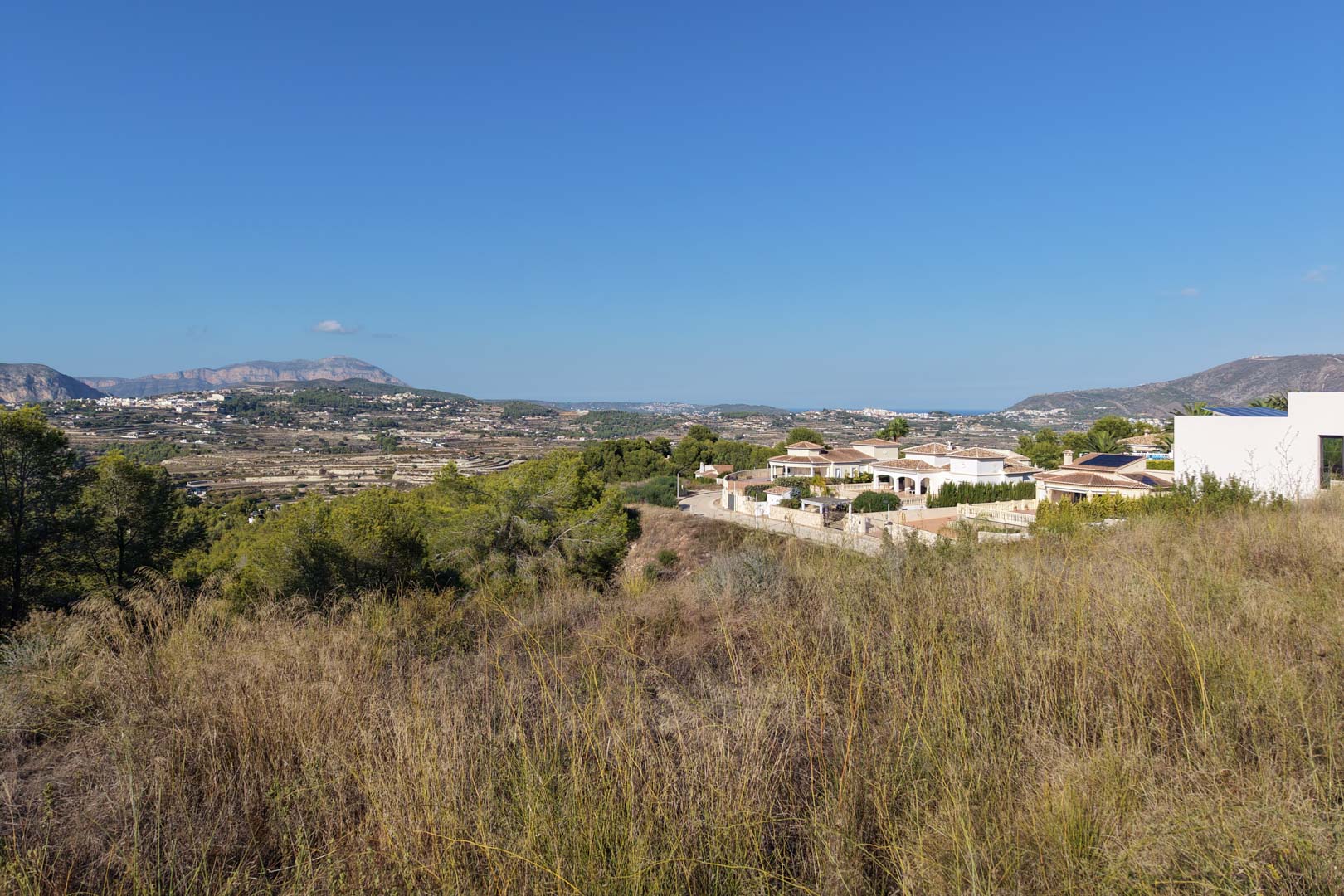Elevated view of the urban plot with wild vegetation, offering open vistas of the valley, distant mountains, and Mediterranean-style villas.