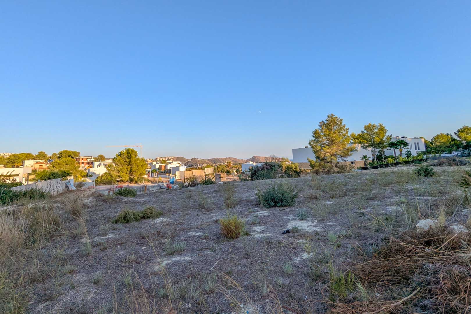 Flat urban plot in El Tesoro featuring open valley views and native vegetation, surrounded by contemporary villas in a developing residential neighborhood.