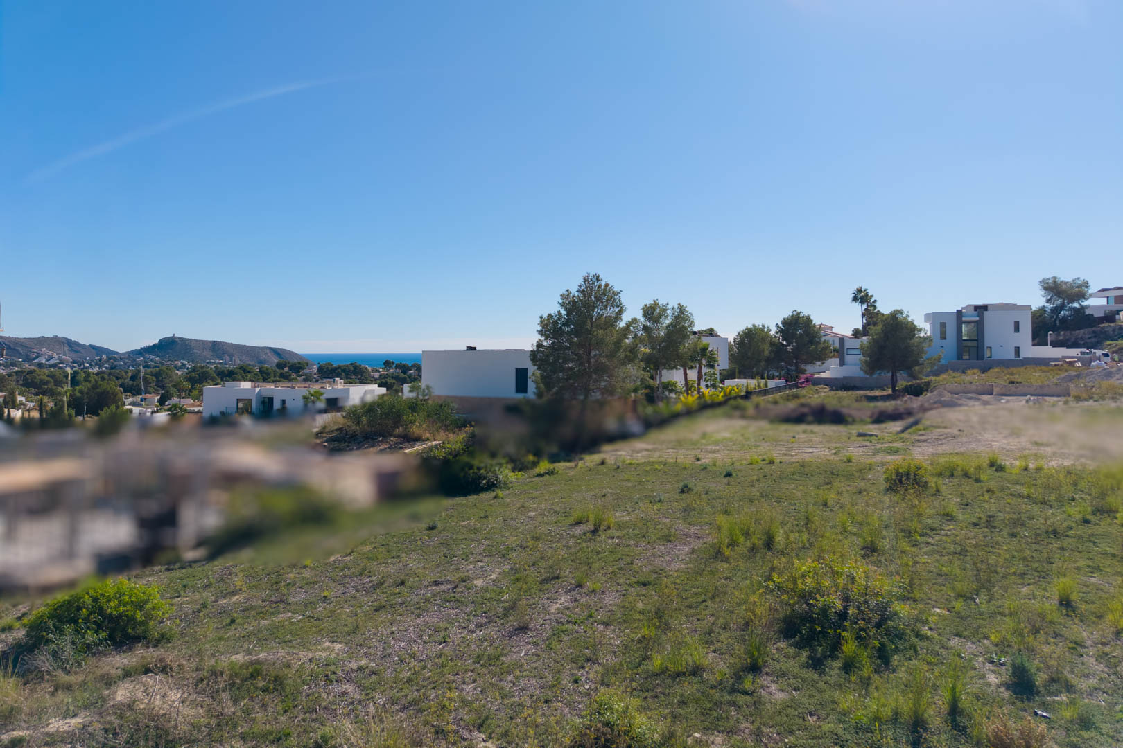 Flat urban plot in El Tesoro, Moraira, featuring open valley views and distant sea glimpses, surrounded by modern architectural villas.