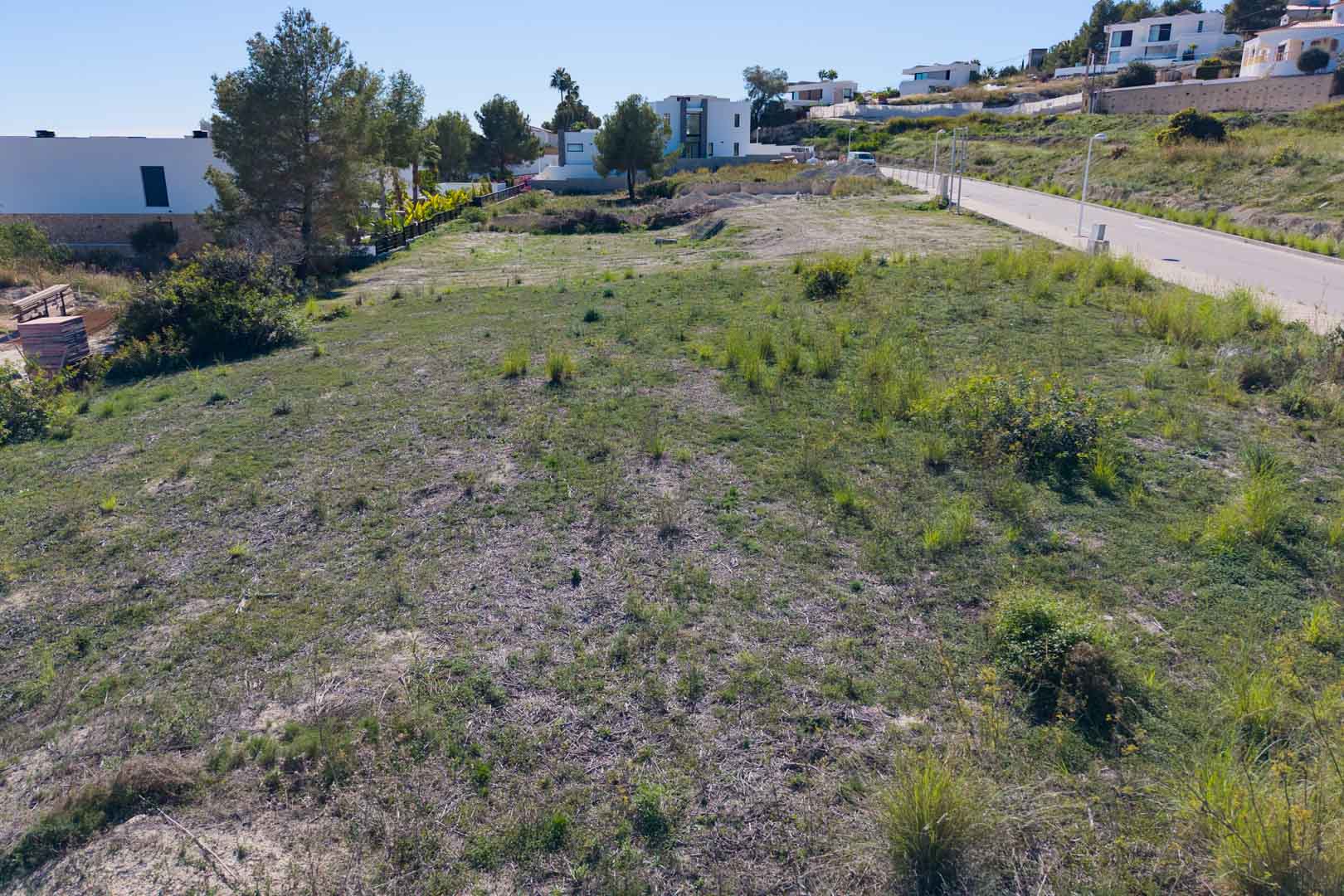 Flat urban plot in El Tesoro, Moraira, featuring paved road access and proximity to contemporary villas. The terrain offers open valley views and clear boundaries.