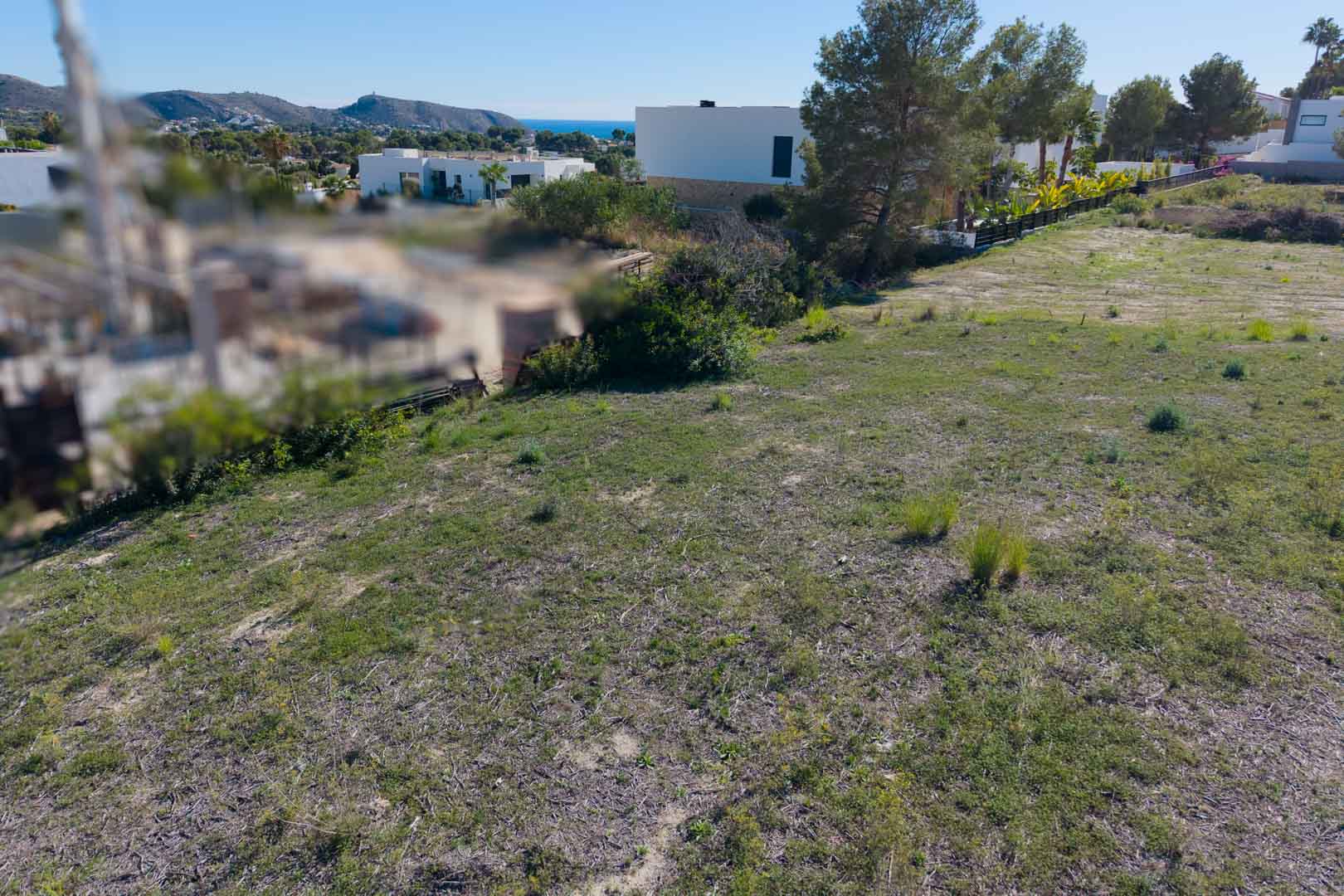 Flat urban plot in El Tesoro, Moraira, offering open valley and Mediterranean Sea views, surrounded by contemporary villas and native vegetation.