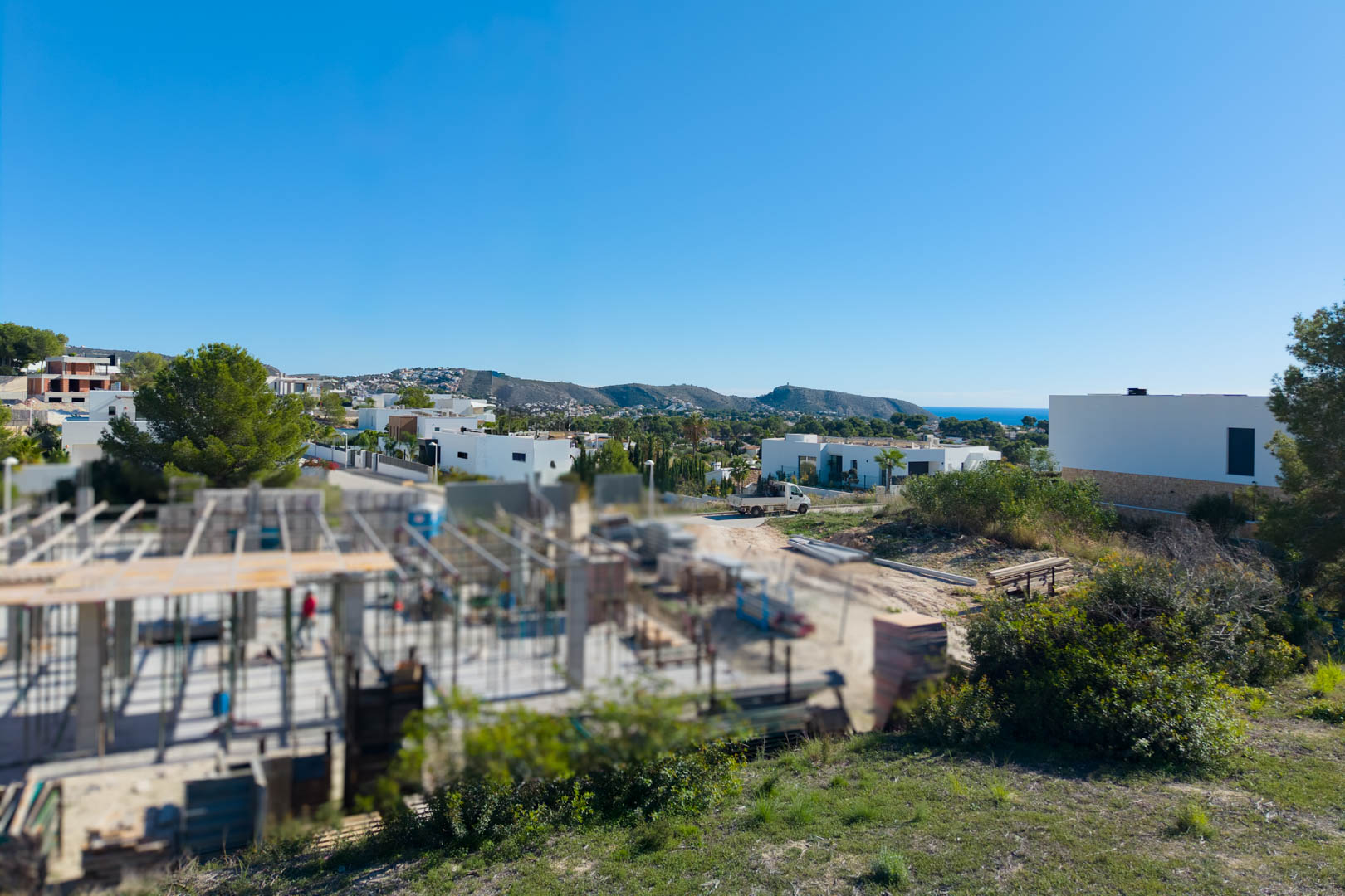 Panoramic view from the El Tesoro plot, featuring modern residential architecture, valley vistas, and a glimpse of the Mediterranean Sea on the horizon.