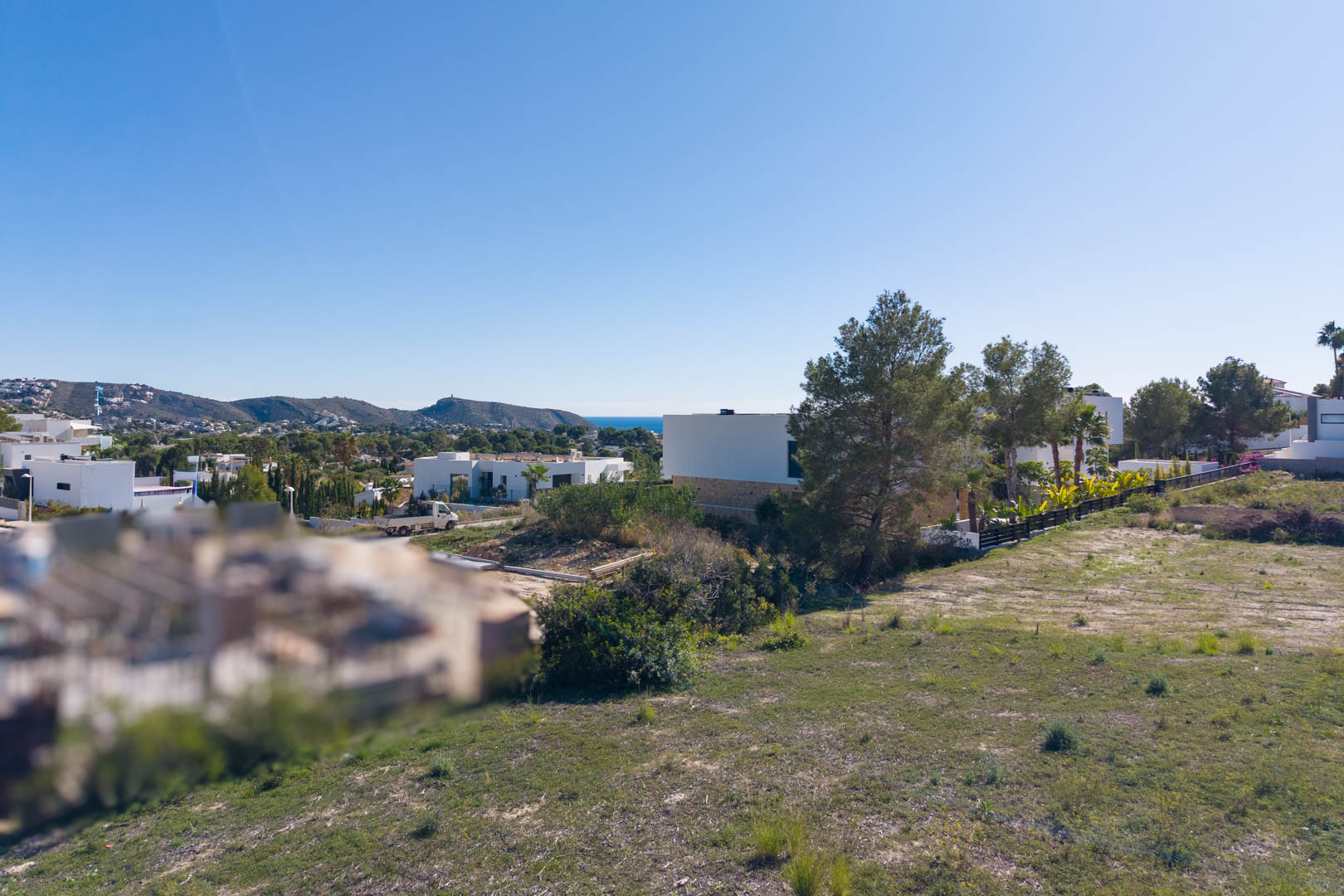 Panoramic view from the urban plot in El Tesoro, featuring flat terrain, surrounding modern villas, and clear vistas toward the valley and Mediterranean Sea.