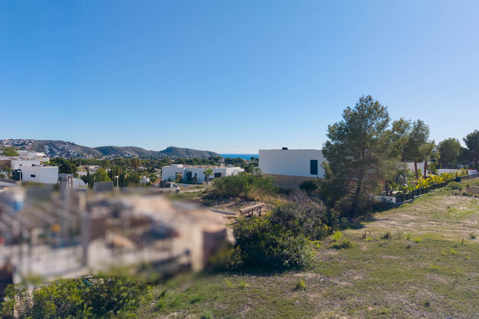 Panoramic view from the urban plot in El Tesoro, featuring level ground, surrounding modern villas, and clear views toward the valley and the Mediterranean Sea.