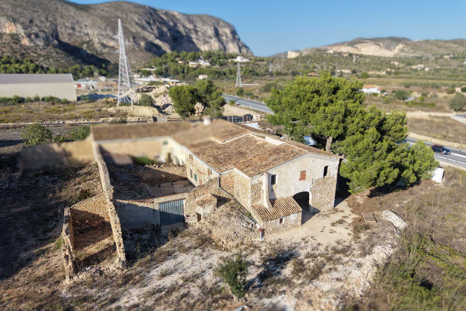 Aerial view of the traditional stone farmhouse featuring original clay tile roofs and outbuildings set against a rugged mountain backdrop.