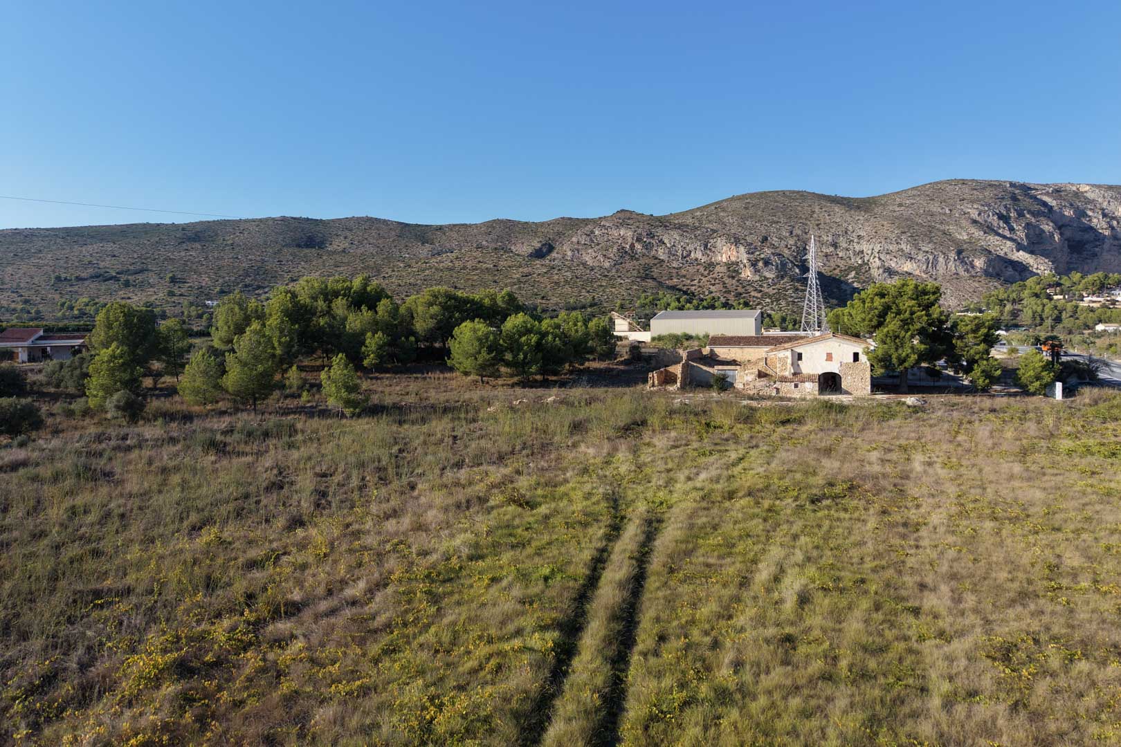 Aerial view of the traditional stone house and its expansive flat plot, surrounded by Mediterranean vegetation with the Teulada mountains in the background.