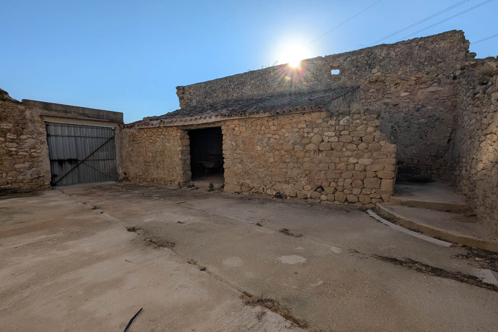 Exterior view of the traditional stone outbuildings and former stables, featuring original masonry walls and a spacious concrete courtyard area.