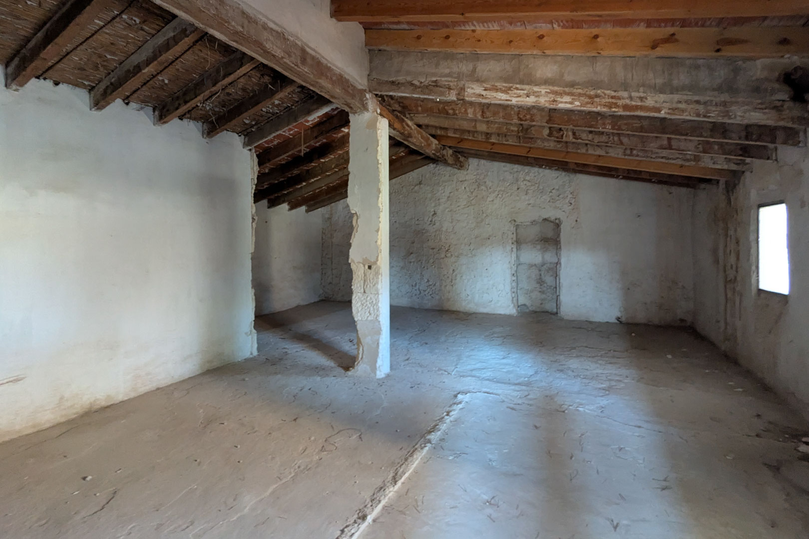 Open-plan upper level showcasing original almond wood beams, cane ceilings, and lime-washed stone walls with a side window for natural light.