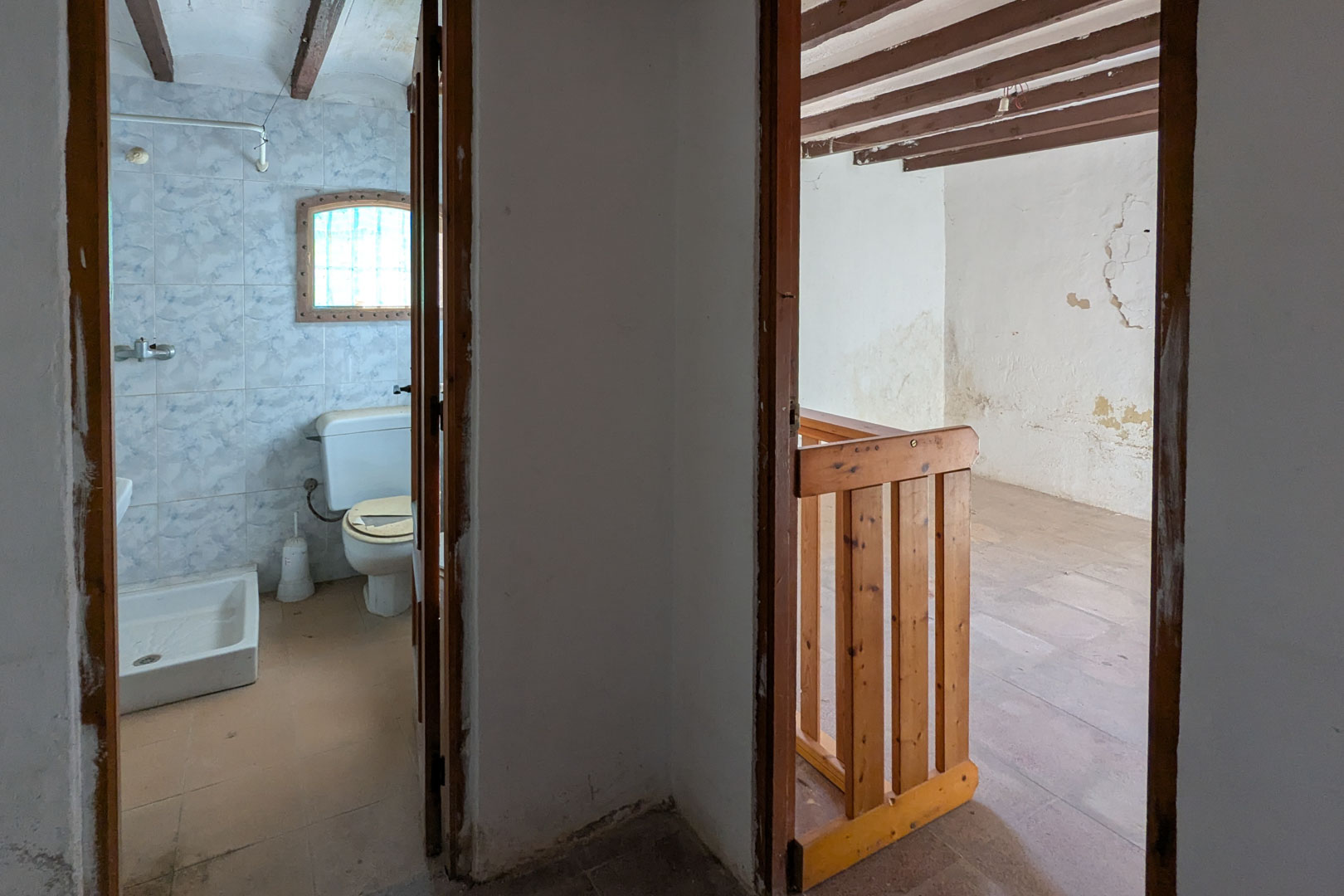 Upper floor view showing a tiled bathroom and an adjacent room featuring exposed wooden ceiling beams and a rustic pine railing.