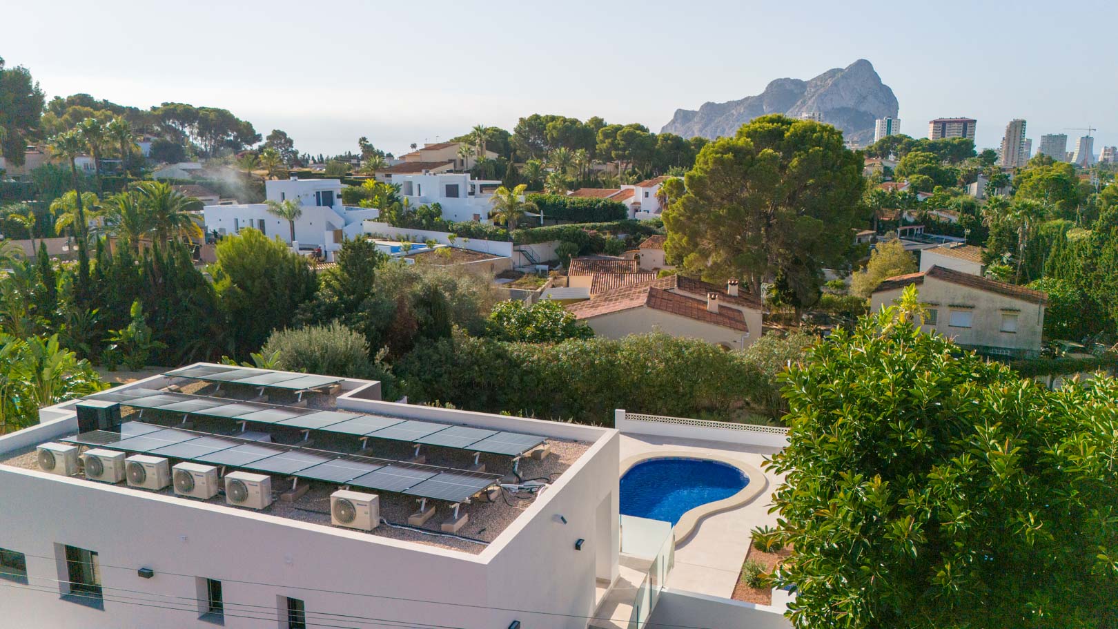 Aerial perspective featuring the rooftop photovoltaic system, air conditioning units, private swimming pool, and views of the Peñón de Ifach.