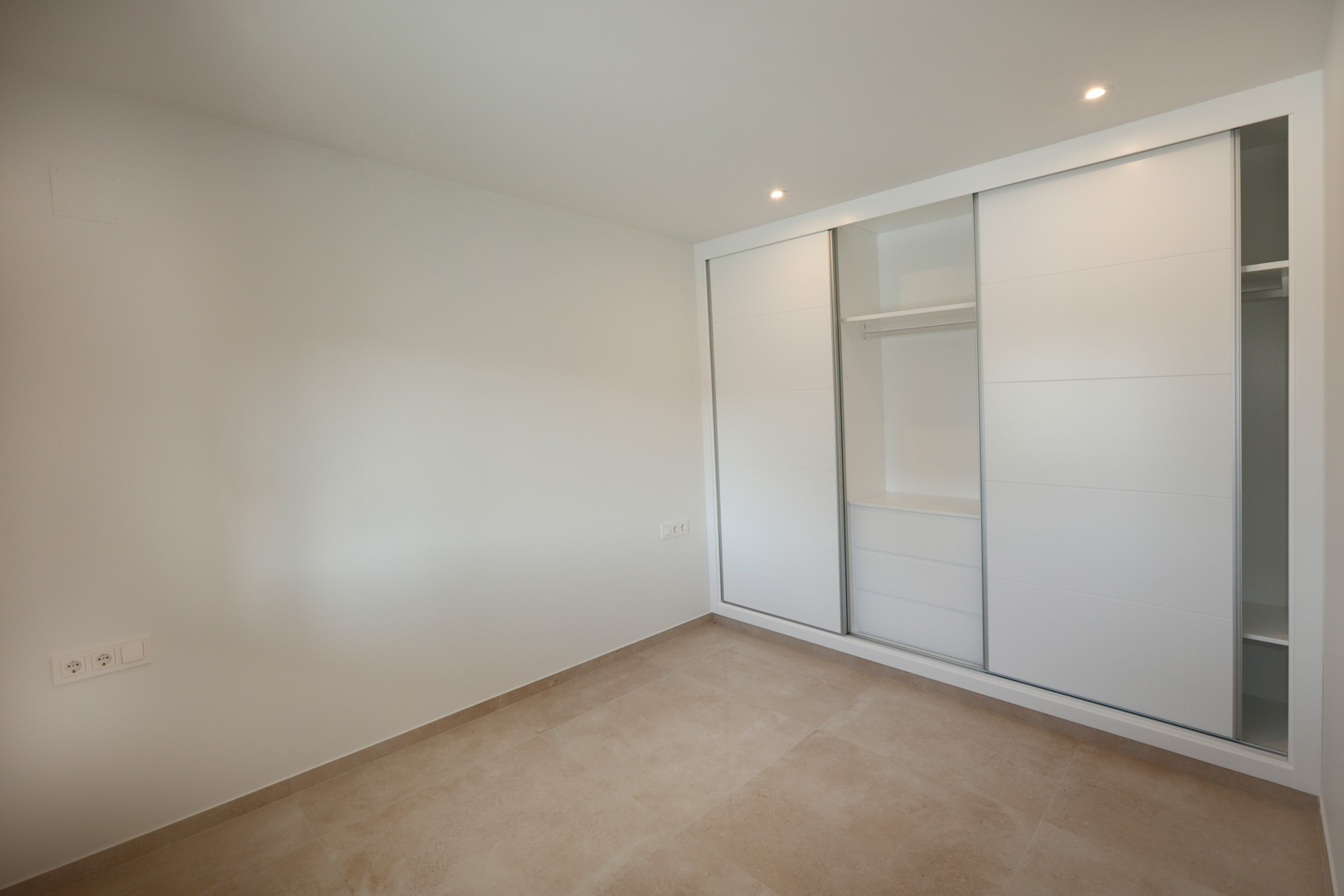 Bedroom featuring a built-in wardrobe with white lacquered sliding doors, porcelain stoneware flooring, and recessed LED ceiling lighting.