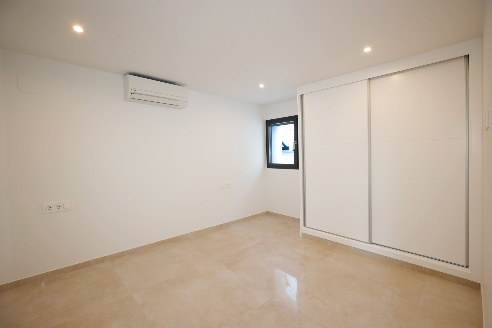 Bedroom featuring a white sliding-door wardrobe, polished porcelain tile flooring, split air conditioning, and recessed LED ceiling spotlights.