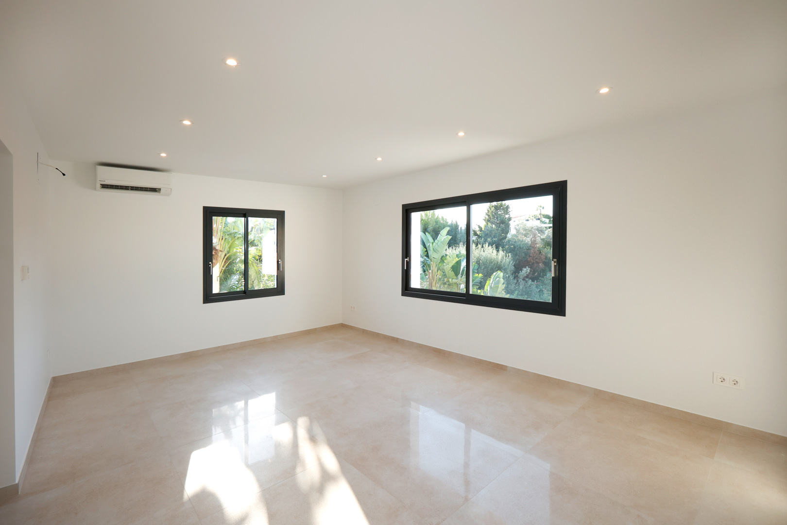 Bright room featuring polished porcelain tile flooring, recessed LED lighting, split air conditioning, and black aluminum windows overlooking the garden.