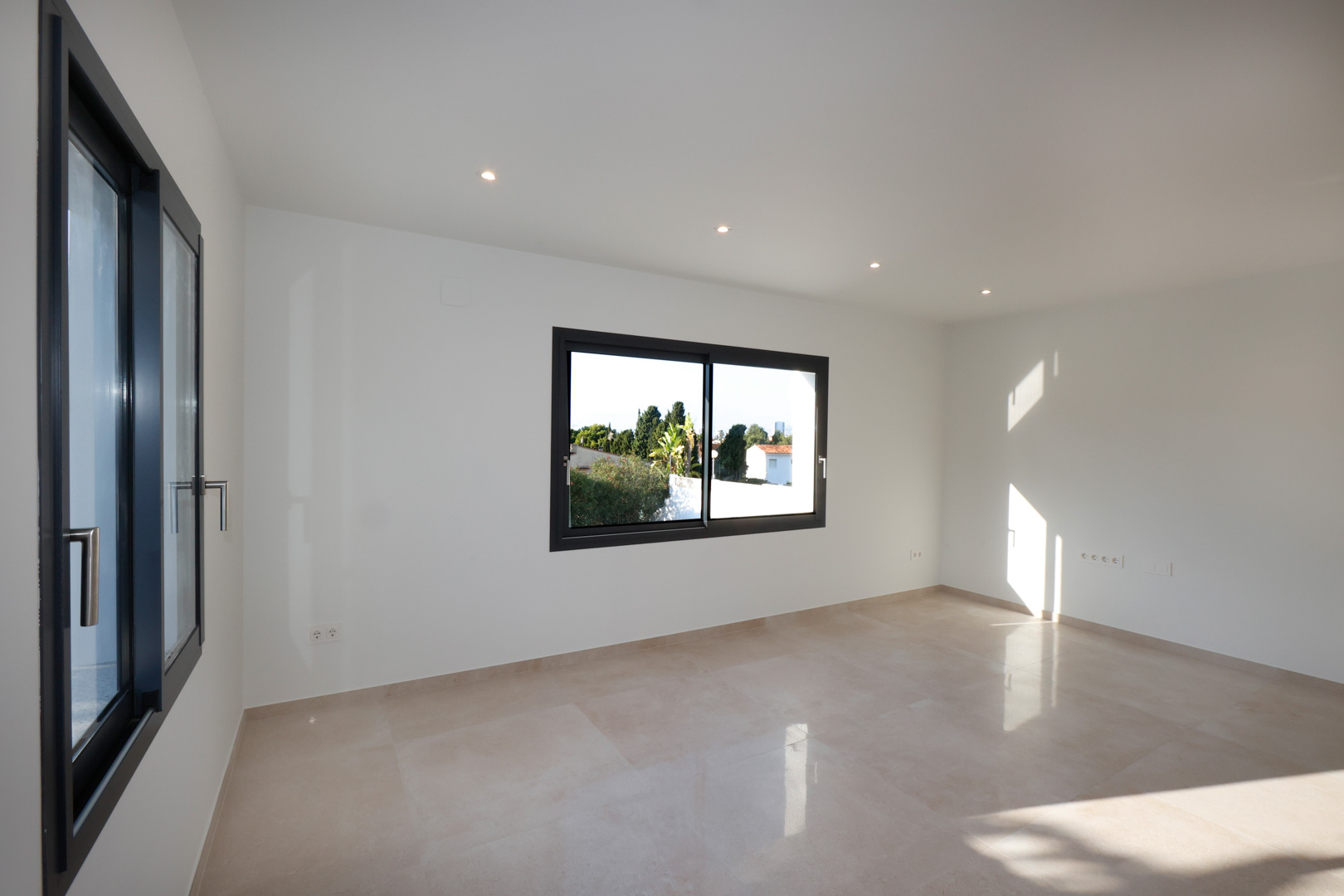 Bright room featuring porcelain stoneware flooring, anthracite Technal aluminum windows, and recessed LED ceiling lighting.