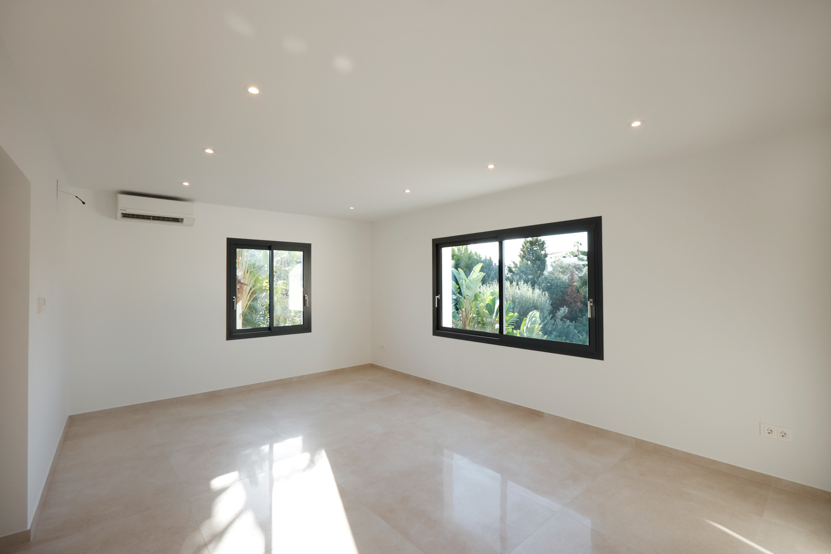 Bright room featuring porcelain tile flooring, recessed LED lighting, split air conditioning, and Technal windows overlooking the garden.