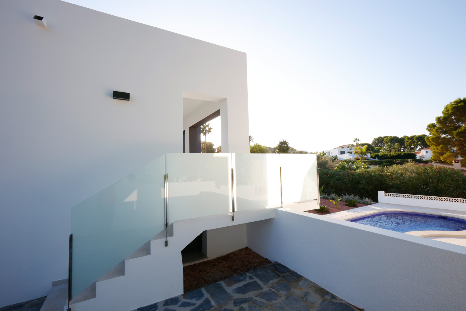 Exterior staircase with steel and glass railings connecting the pool area to the upper entrance of the modern white villa.