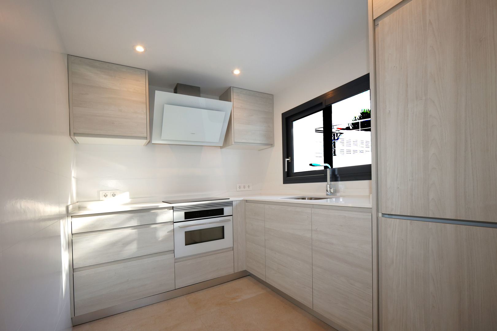 Functional kitchen with light wood cabinetry, white Silestone countertops, induction hob, Bosch oven, and a decorative extractor hood.
