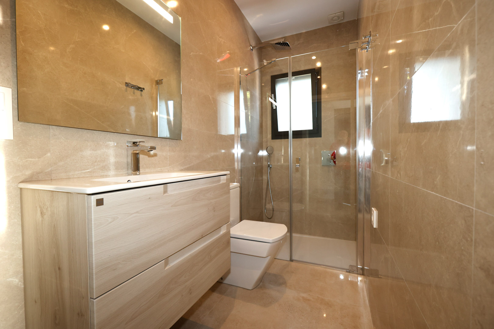 Modern bathroom featuring a light wood vanity, marble-effect porcelain wall tiles, and a walk-in glass shower with chrome fixtures.