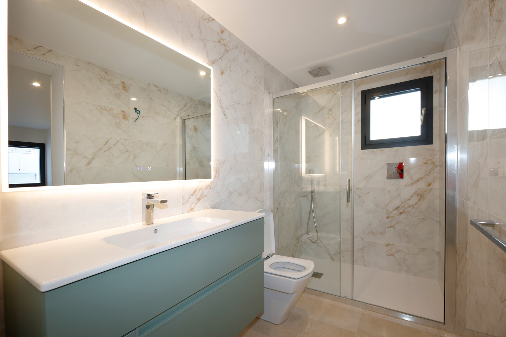 Modern bathroom featuring a sage green vanity, LED-backlit mirror, and a walk-in glass shower with marble-effect porcelain tiling.