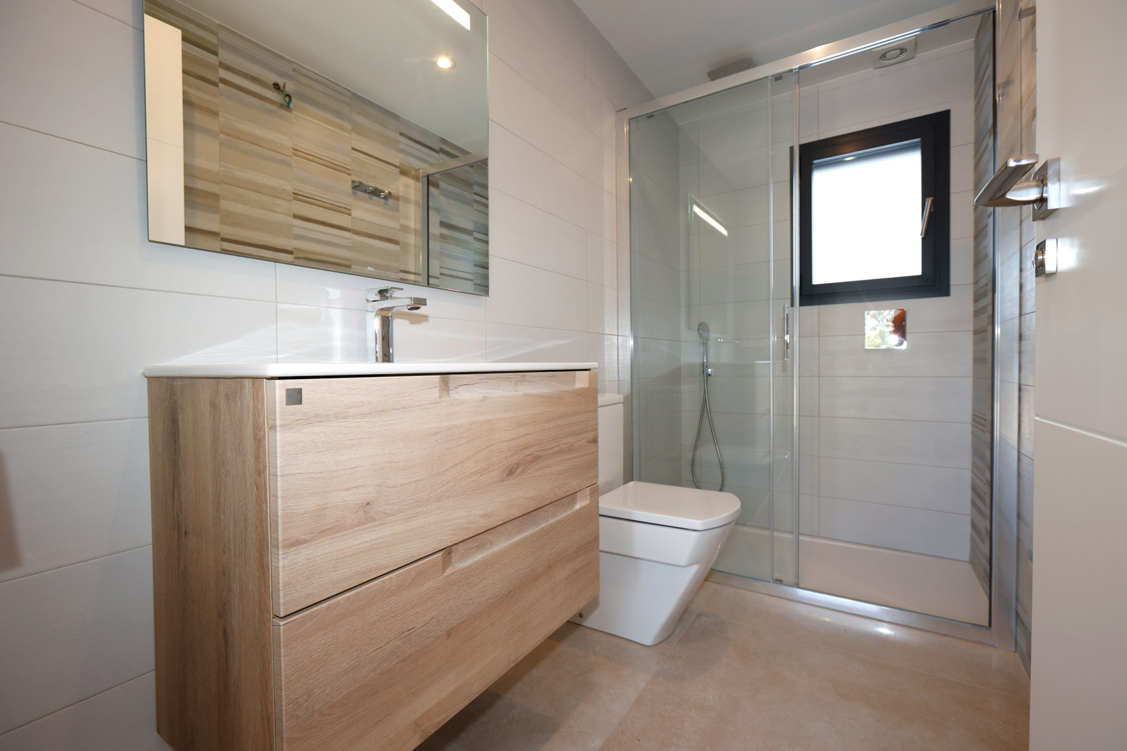 Modern bathroom with a wood-effect vanity, glass shower partition, and white wall tiles. Features a black-framed window and porcelain flooring.