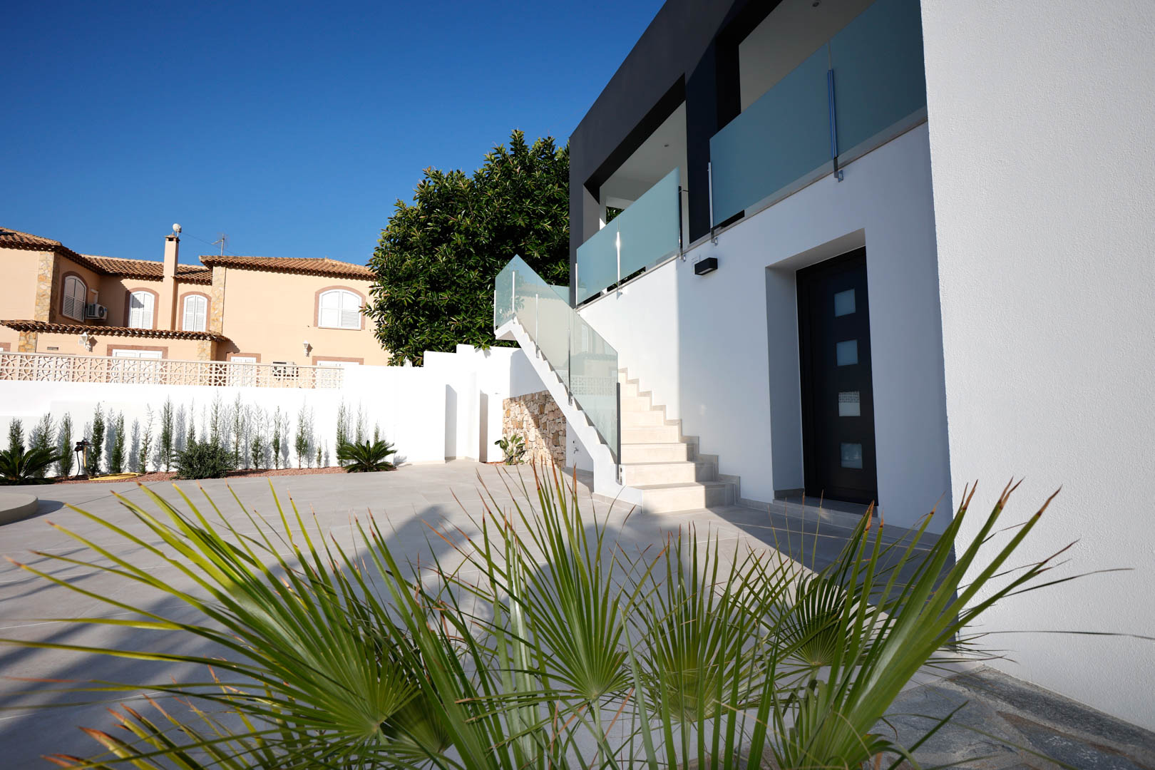 Modern facade featuring an exterior staircase with glass railings, porcelain tiled terrace, and independent access door under a clear sky.