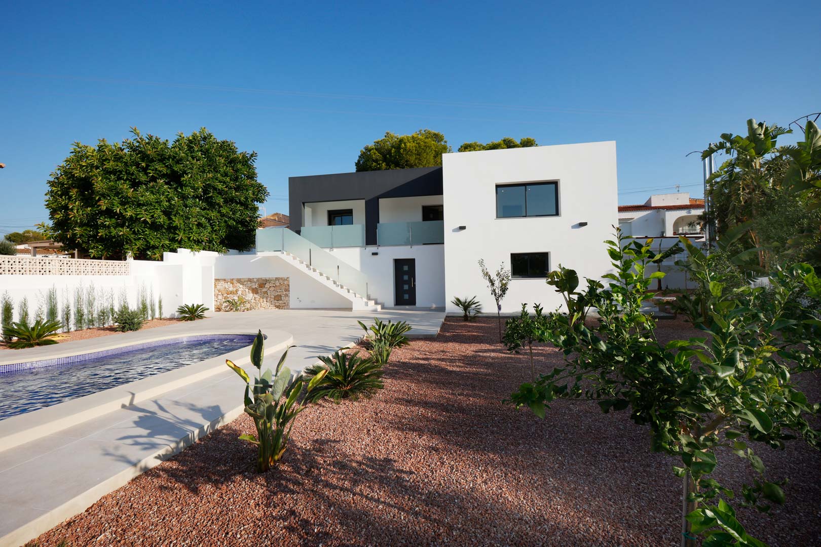 Modern facade with swimming pool, red marble gravel garden, and external staircase with steel and glass railings. Features natural stone walls and Technal carpentry.