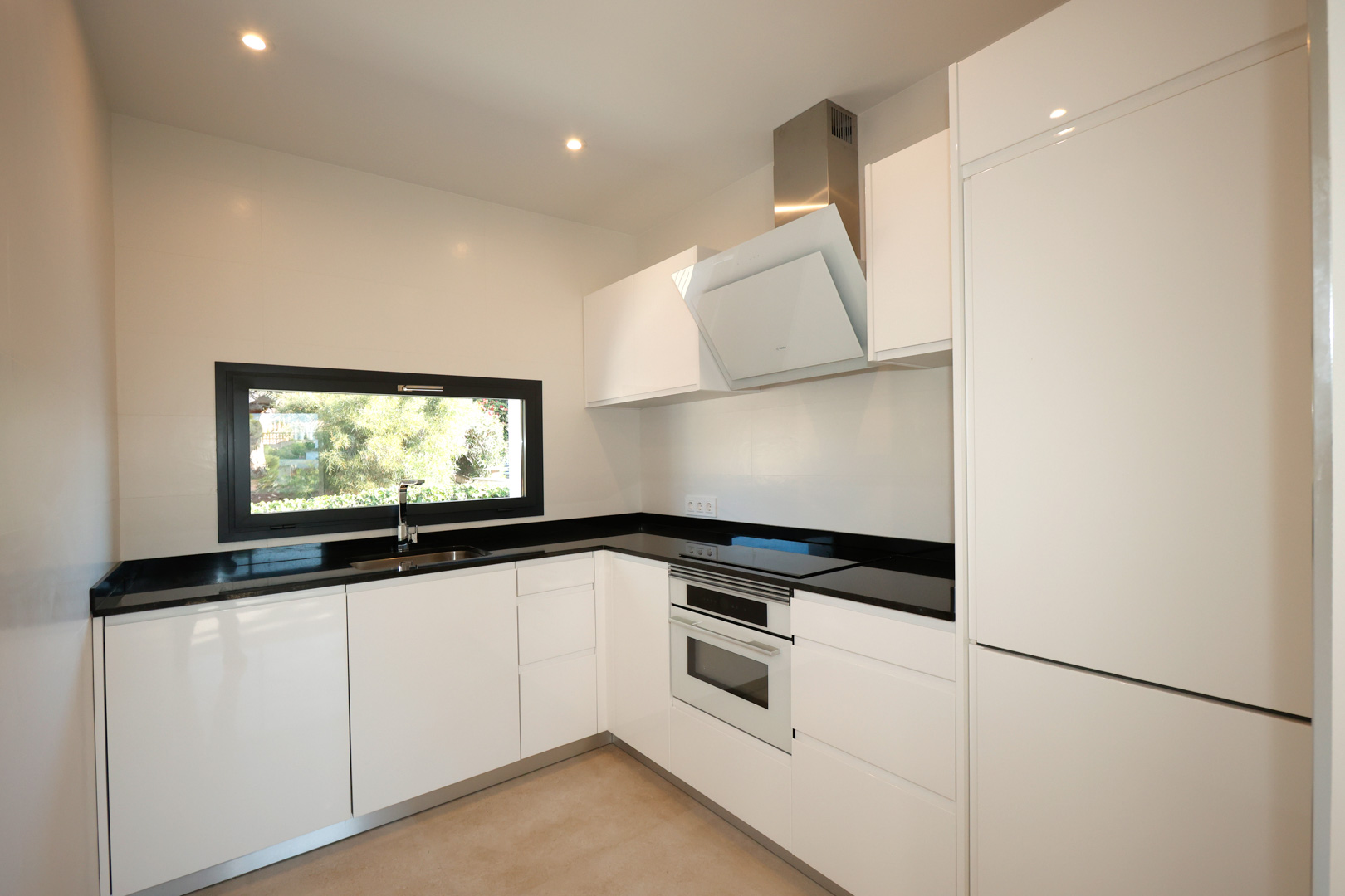 Modern kitchen featuring white cabinetry, black Silestone countertops, integrated Bosch appliances, and a horizontal window with garden views.