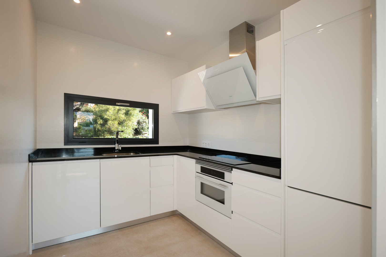 Modern kitchen featuring white lacquered cabinetry, black Silestone countertops, integrated Bosch appliances, and a window with garden views.