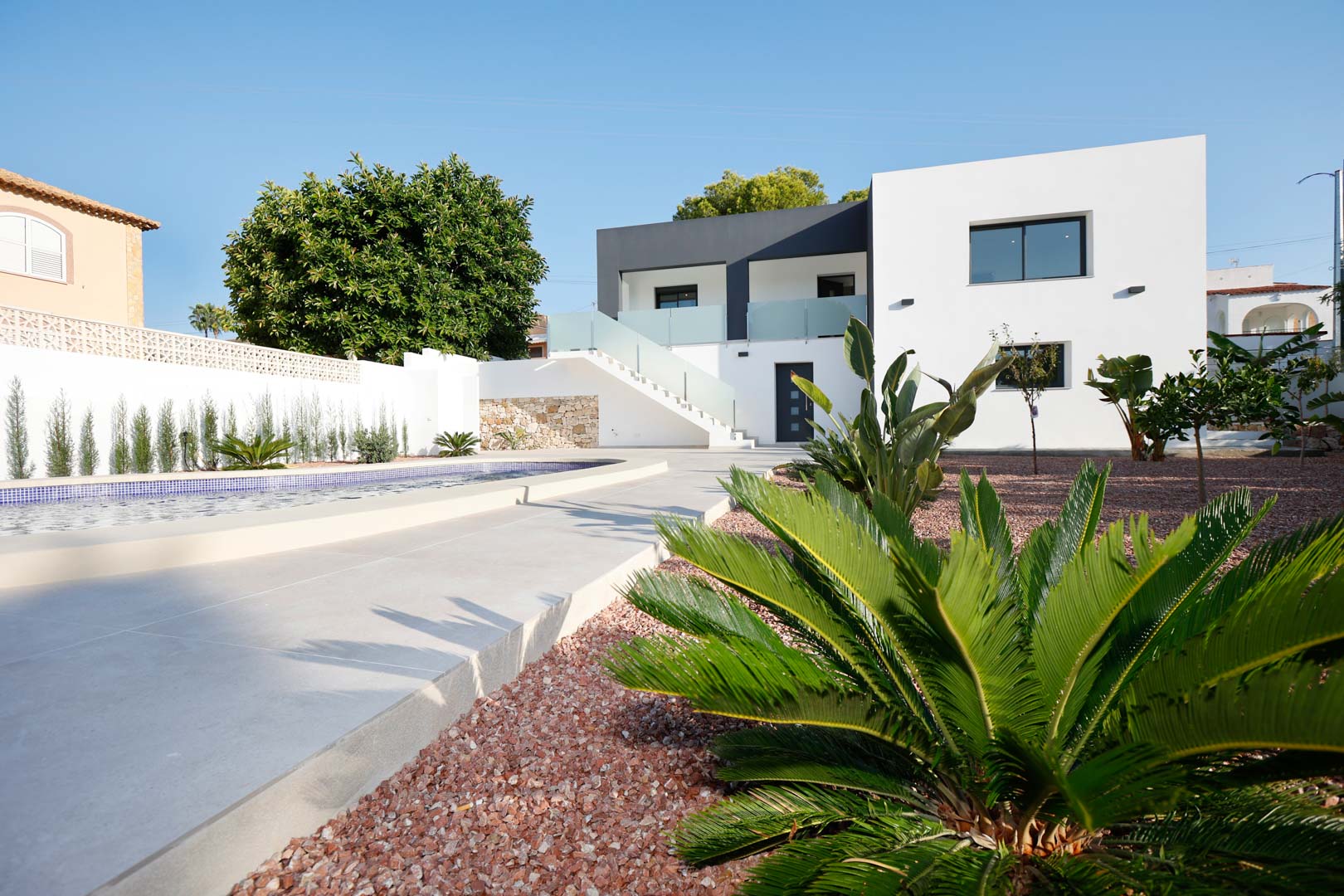 Modern two-story villa featuring a swimming pool, red marble gravel garden, and an external staircase with glass railings leading to the upper floor.