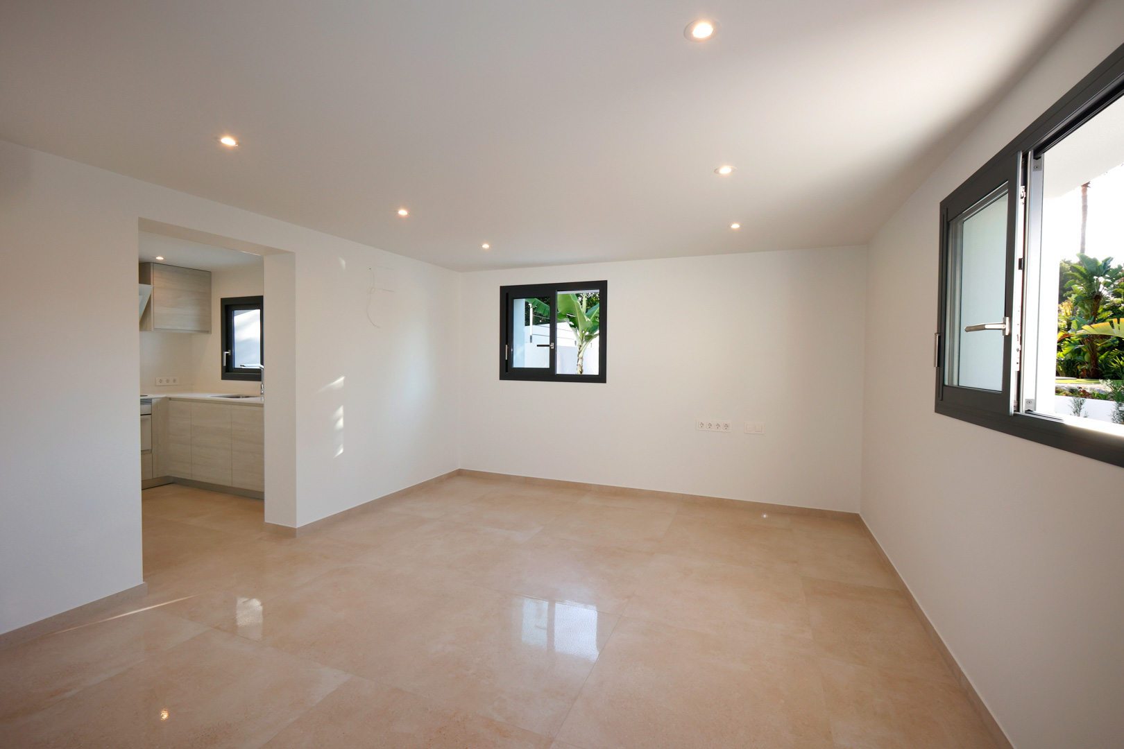 Open-plan living area featuring polished porcelain tile flooring, recessed LED lighting, and Technal aluminum windows with views of the garden.