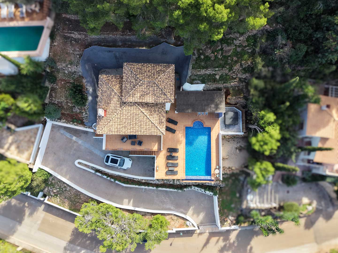 Aerial top-down view of the villa featuring a terracotta tiled roof, rectangular pool, sun terrace with loungers, outdoor jacuzzi, and private driveway nestled in greenery.