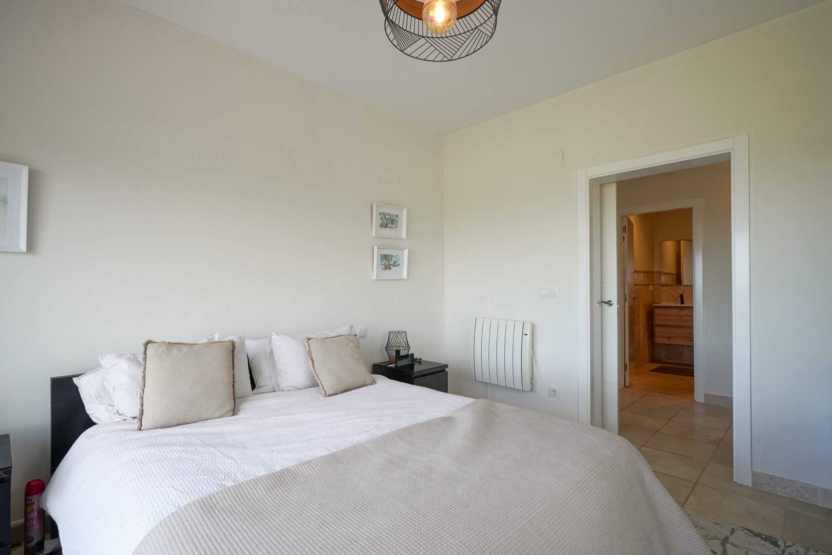 Bright bedroom featuring ceramic tile flooring, a double bed, and direct access to an en-suite bathroom. Includes an electric radiator and modern wire pendant lighting.