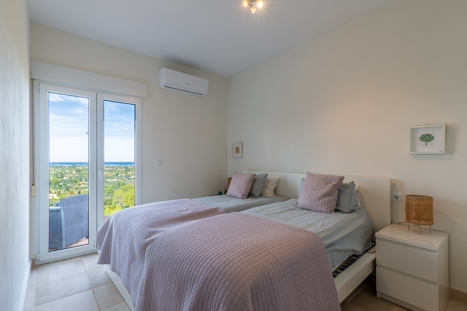 Bright bedroom featuring direct terrace access, split air conditioning, and panoramic views of the Mediterranean coastline and landscape.