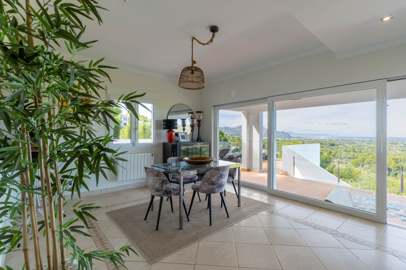 Bright dining area featuring a glass table and sliding doors that open onto a terrace with panoramic sea and mountain views.