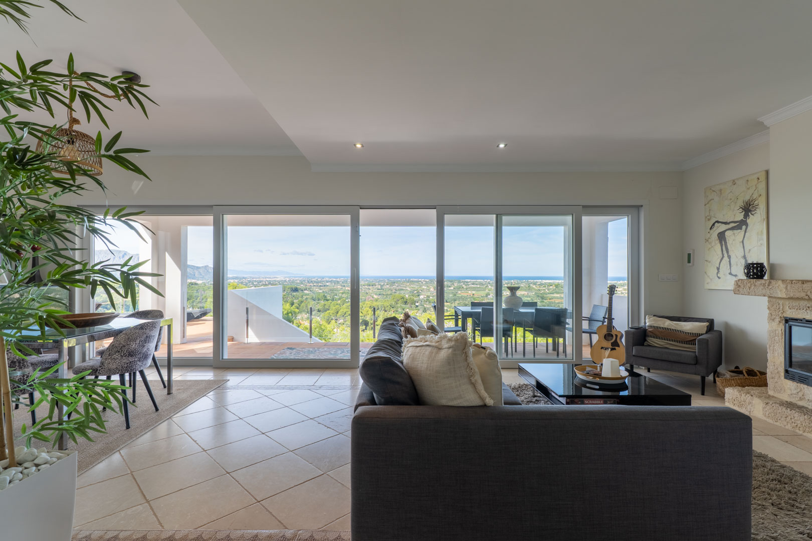 Bright open-plan living area featuring large sliding glass doors with panoramic sea views, a stone fireplace, and direct access to the outdoor terrace.