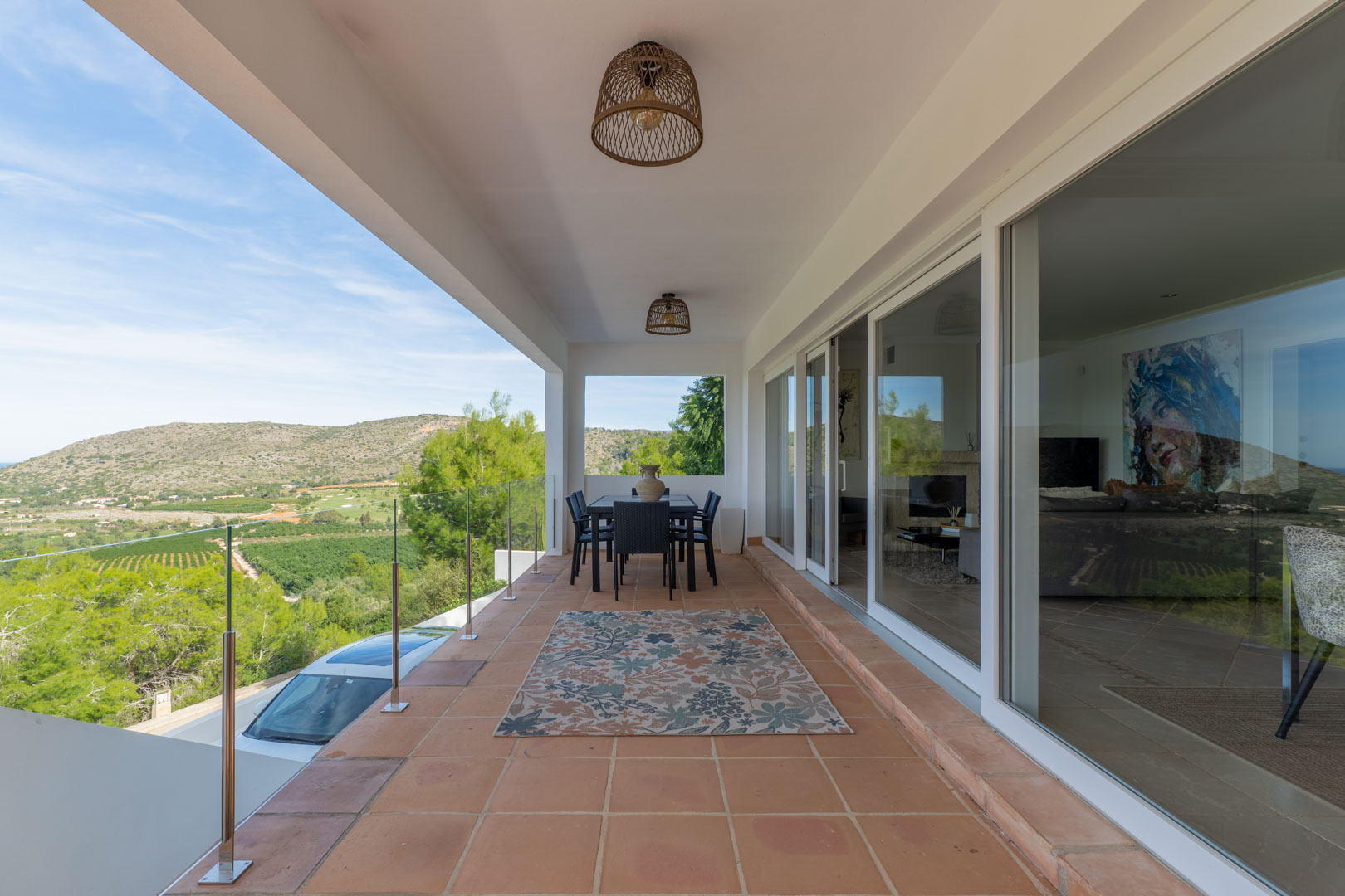 Covered terrace featuring terracotta tiles, glass balustrades, and panoramic golf course views. Includes an outdoor dining area and large sliding glass doors to the interior.