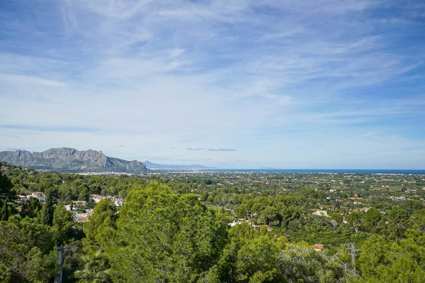 Elevated panoramic views from La Sella overlooking the Montgó mountain range, the lush coastal valley, and the Mediterranean Sea on the horizon.