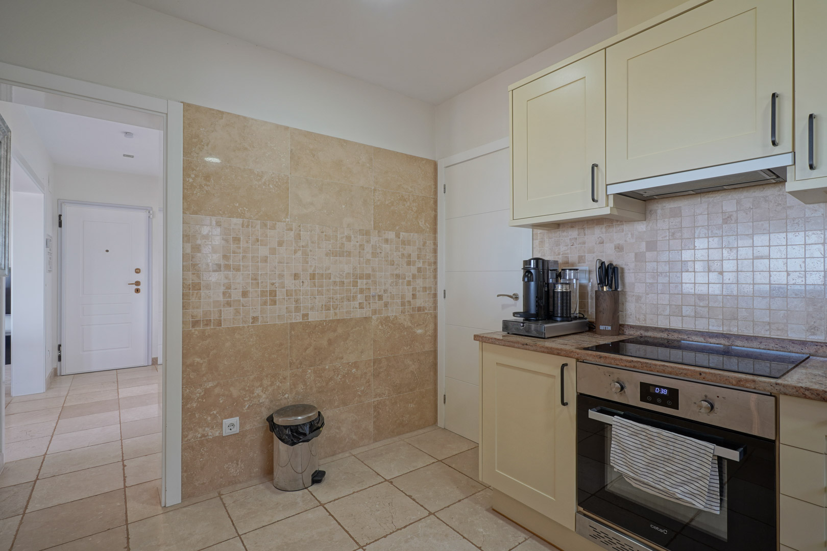Functional kitchen featuring cream cabinetry, granite countertops, and integrated appliances. The wall is finished with natural stone tiling and a mosaic accent strip.