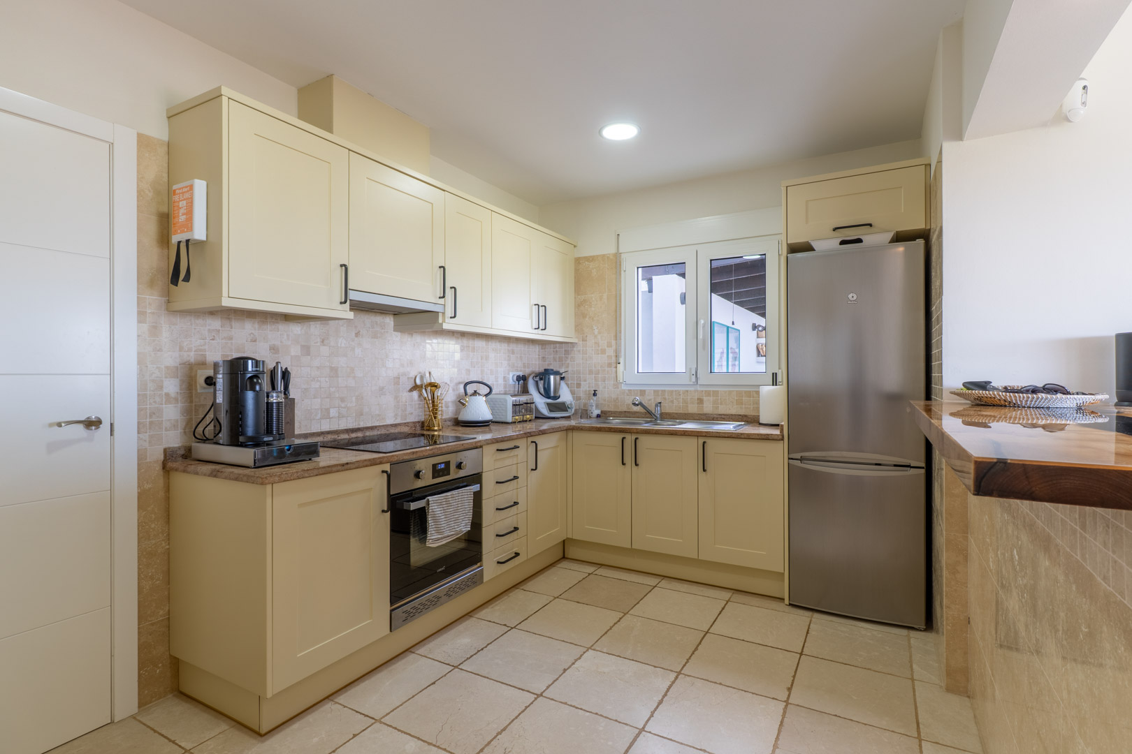 Functional kitchen featuring cream cabinetry, granite countertops, and stainless steel appliances, complemented by a solid wood breakfast bar and tiled backsplash.