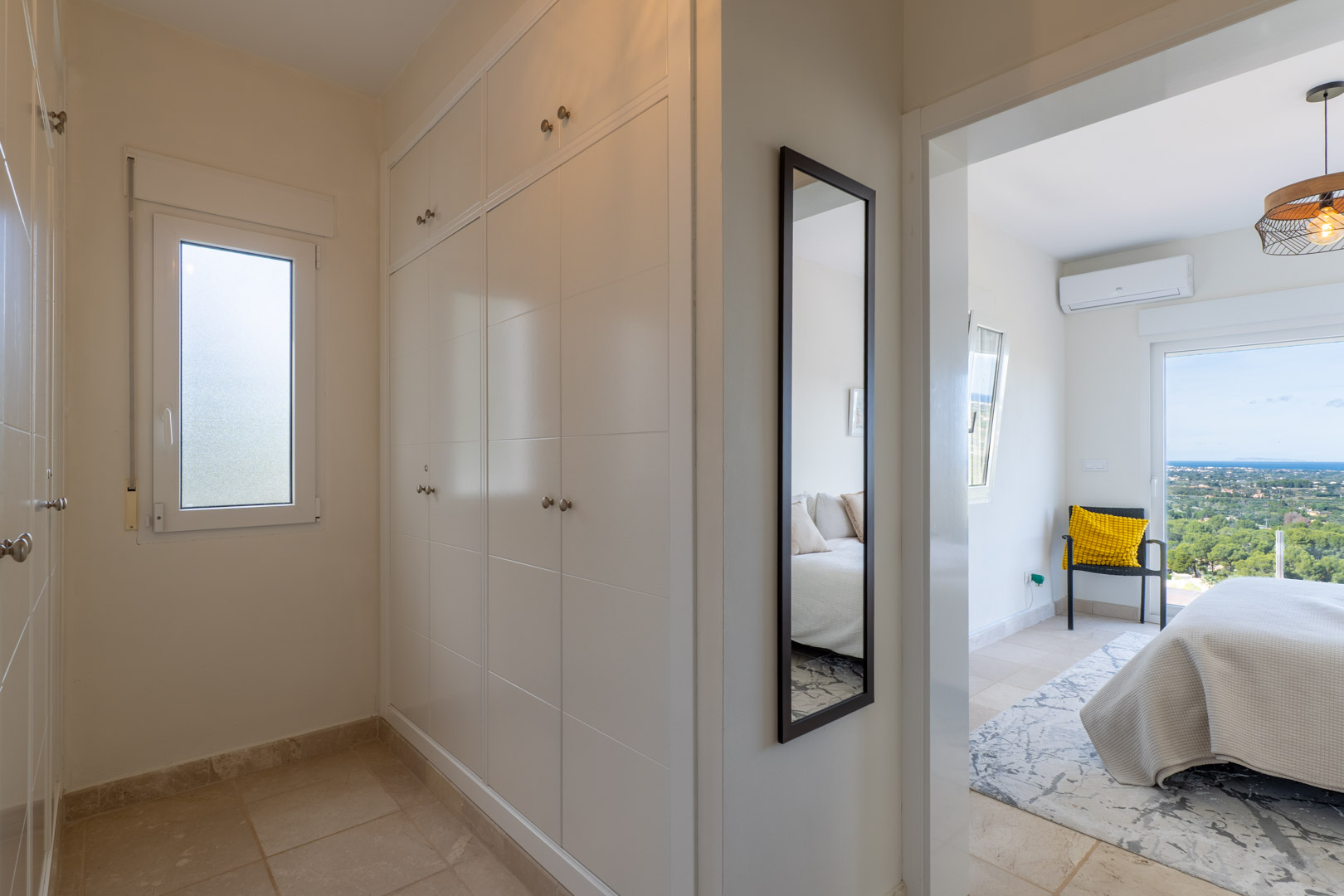 Hallway with white built-in wardrobes and a full-length mirror leading to a bedroom with panoramic sea views and air conditioning.