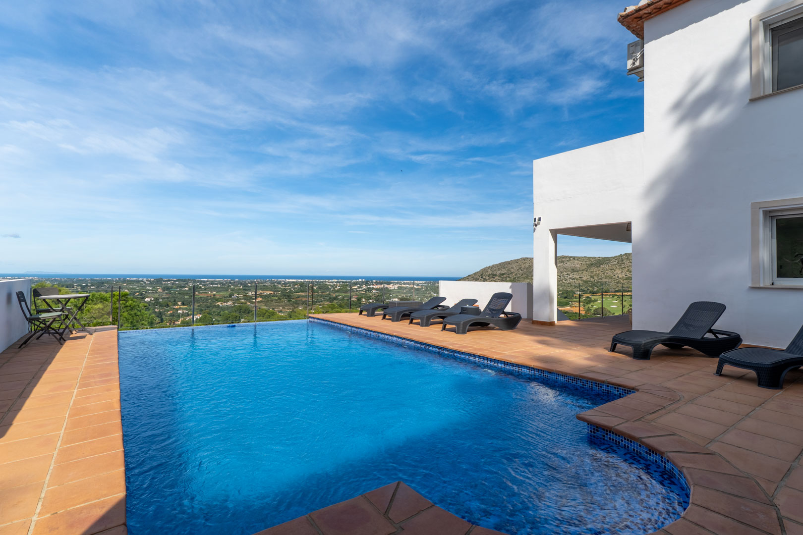 Private swimming pool featuring a terracotta tile terrace, black sun loungers, and glass railings offering panoramic views of the Mediterranean Sea and golf course.