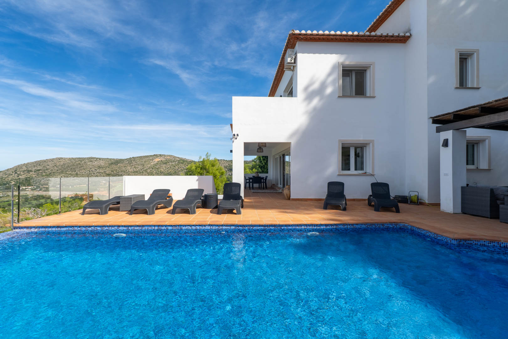 Private swimming pool with blue mosaic tiling, featuring a terracotta terrace with sun loungers and panoramic views of the surrounding hills.
