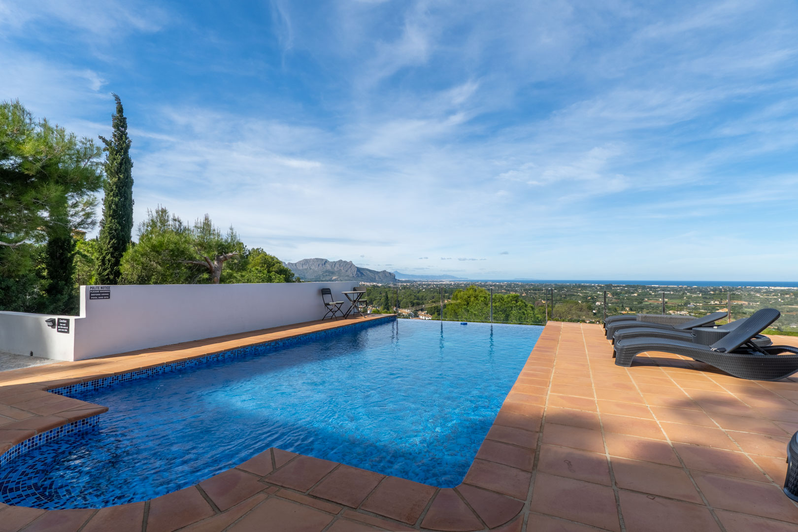Swimming pool with blue mosaic tiling and terracotta terrace, featuring panoramic views of the Mediterranean Sea and the Montgó mountain range.