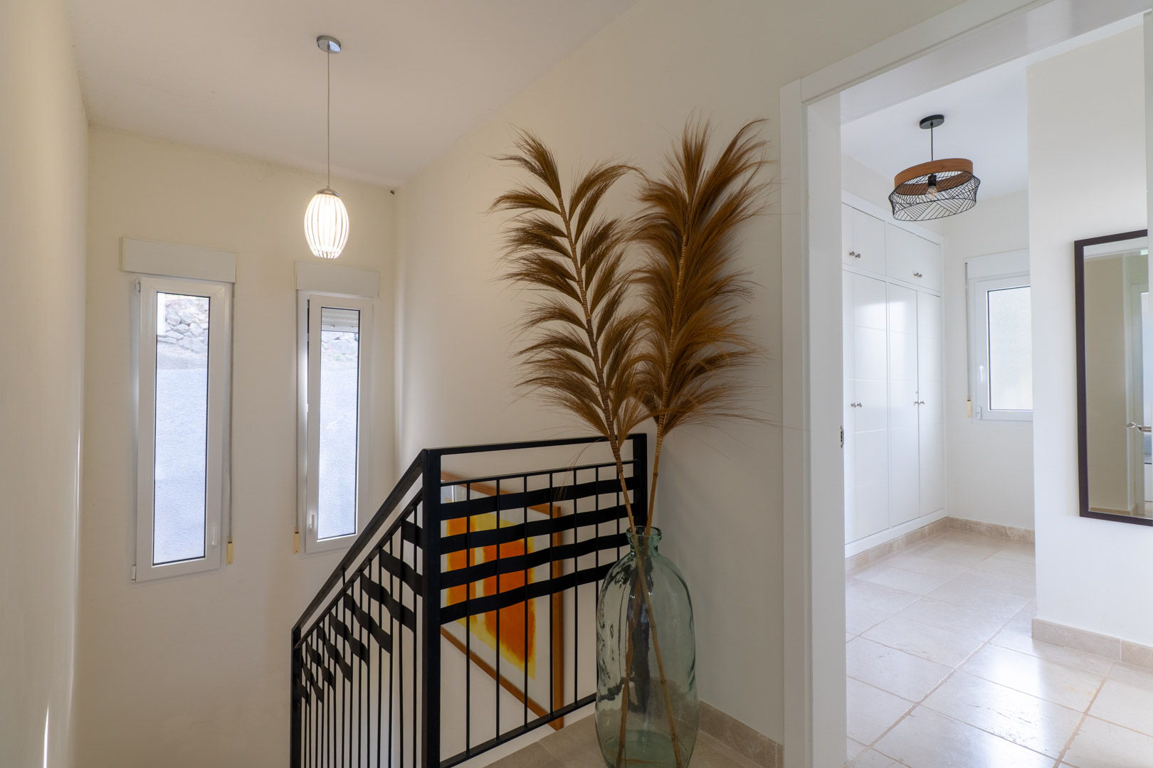 Upper floor landing featuring a black metal staircase railing, neutral tiled floors, and a doorway leading to a room with built-in white wardrobes.