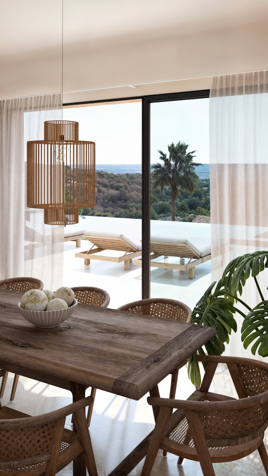 Dining area featuring a solid wood table and slatted pendant light, overlooking the terrace with sun loungers and infinity pool through large glass doors.