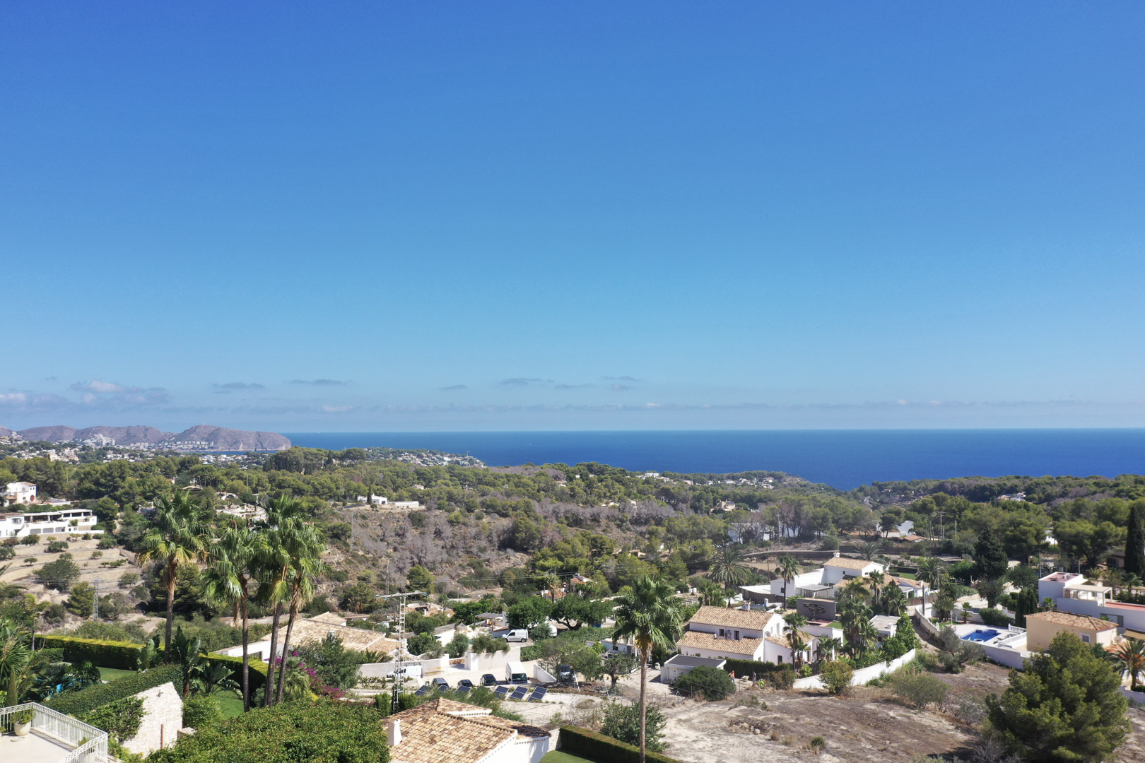 Elevated panoramic view from Racó de Galeno towards the Mediterranean Sea, showcasing coastal vegetation and residential villas in Benissa under a clear sky.